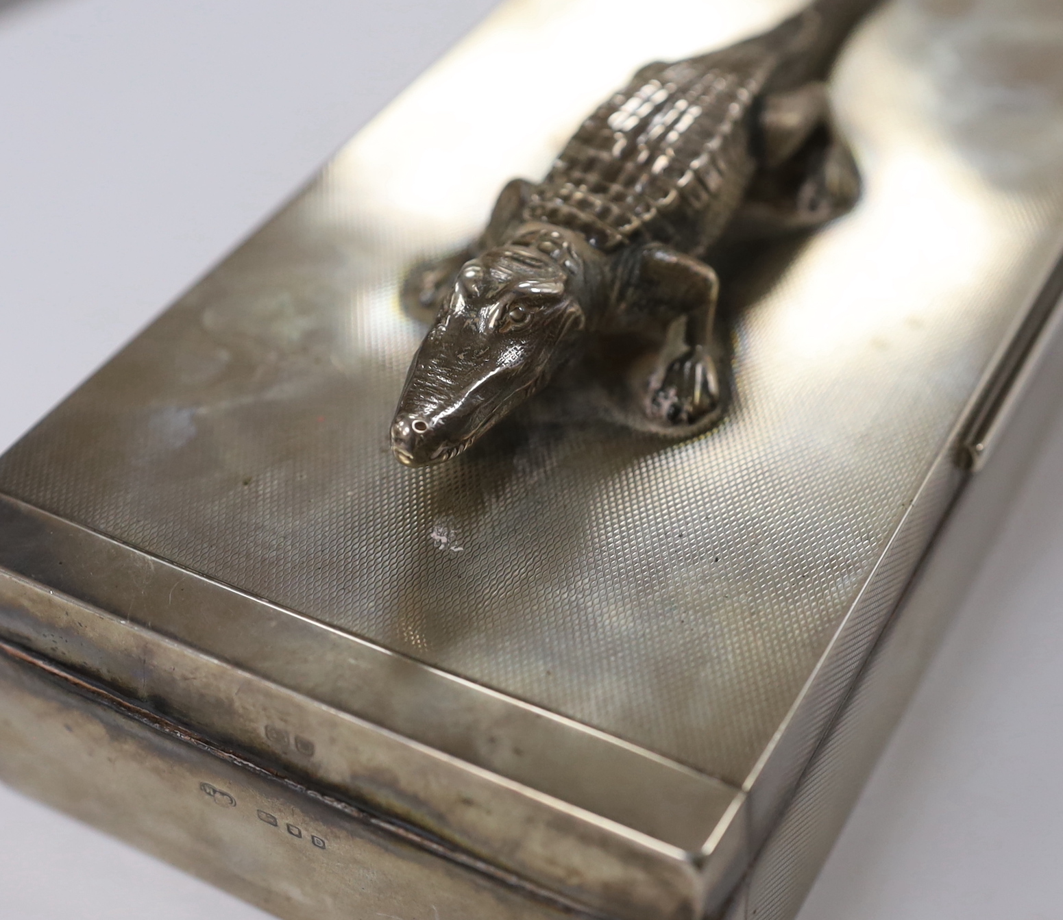 A George VI part engine tuned silver mounted rectangular cigarette box, with white metal crocodile surmount and interior presentation inscription relating to 'Lt. Colonel K.F.G. Stronach', maker Hamilton & Co, London, 19